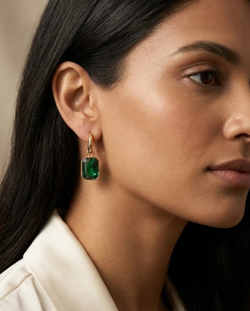 Front view of Élise Emerald Huggies with green stone pendants